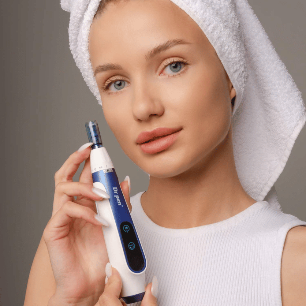 Woman with a towel around her hair holds a Dr. Pen A11 microneedling pen – professional skincare device for smoother and firmer skin.